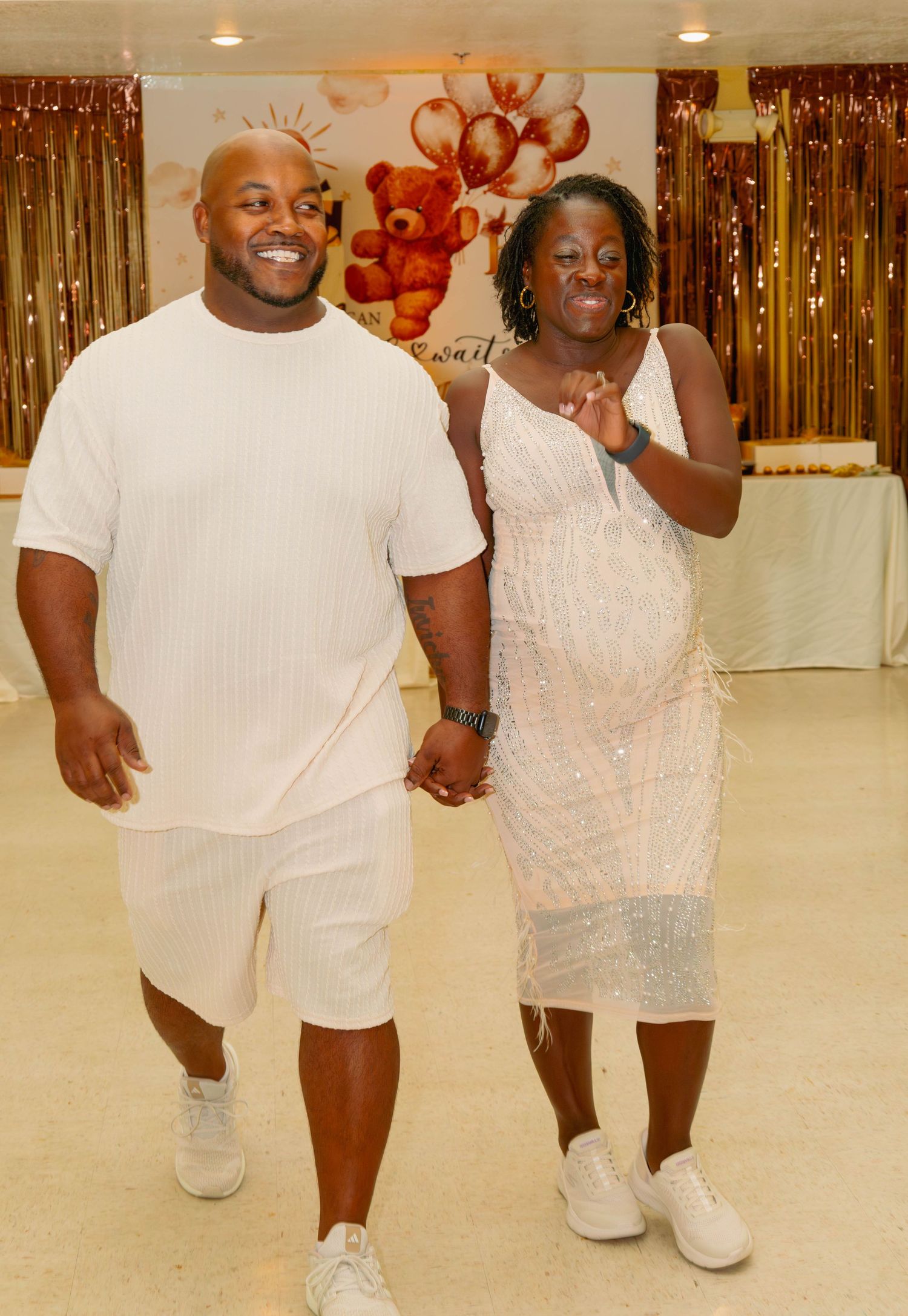 Couple in matching white outfits walking together at a baby shower celebration.