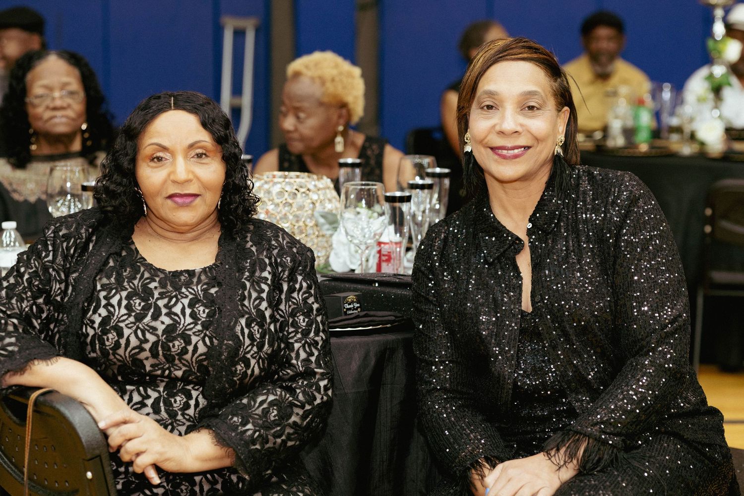 Two women in black lace outfits smile at a formal banquet event.