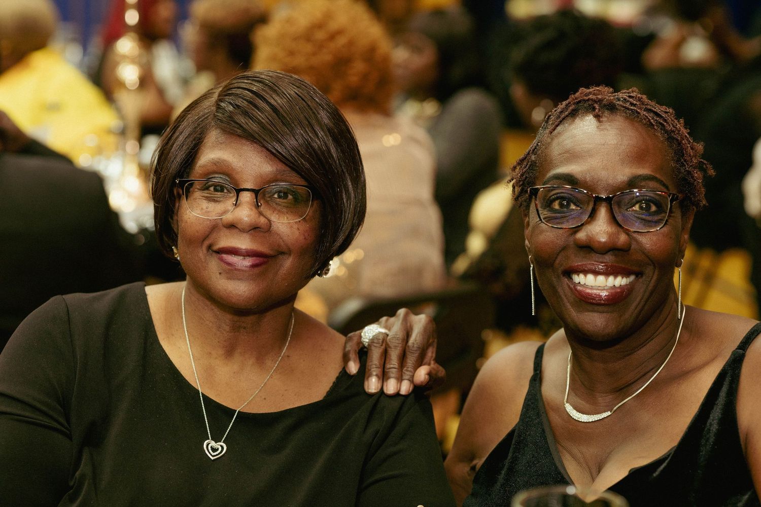Two smiling women pose together at a celebratory dinner event.