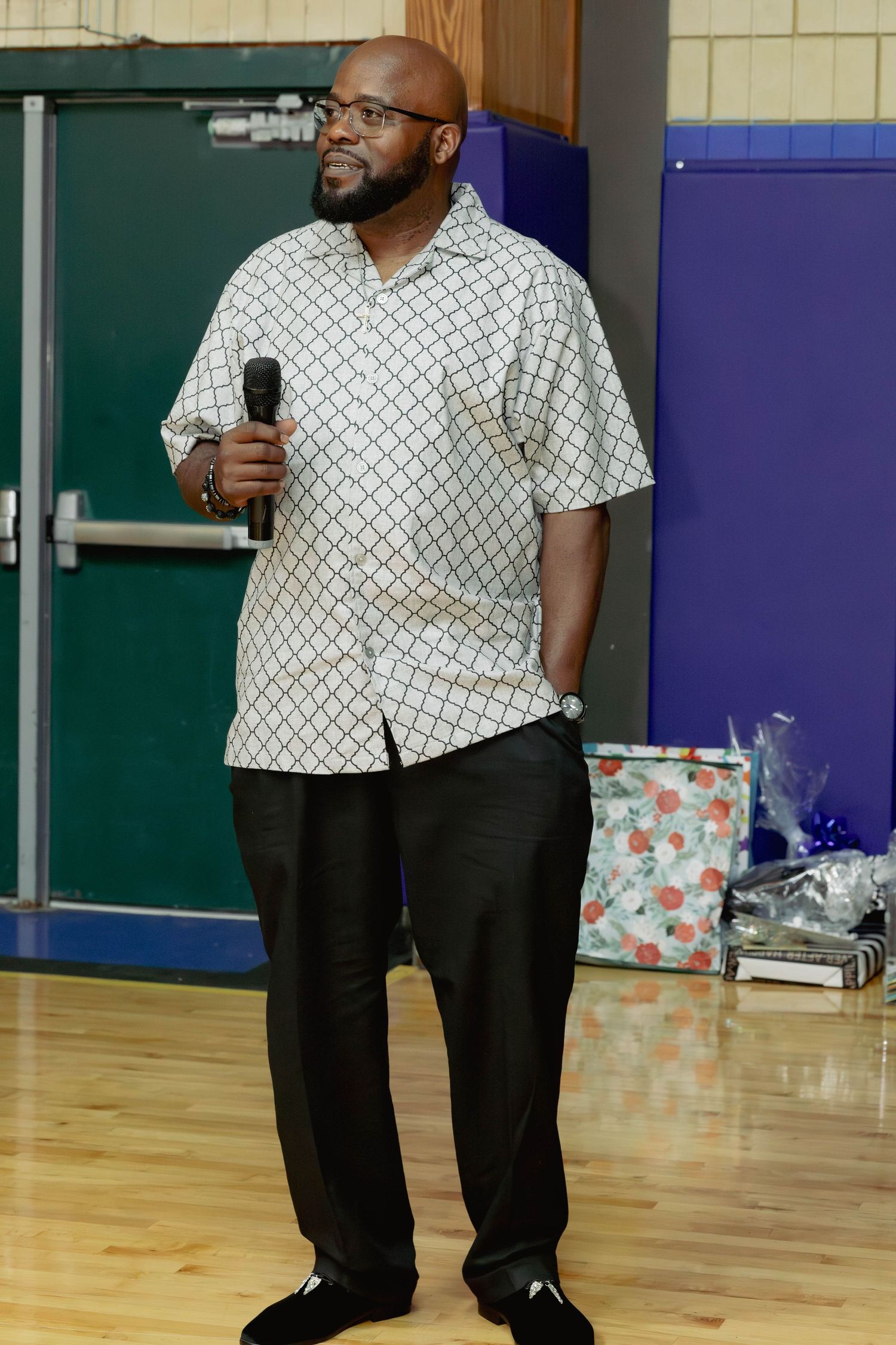 Man in patterned shirt holds microphone while speaking at an indoor celebration.
