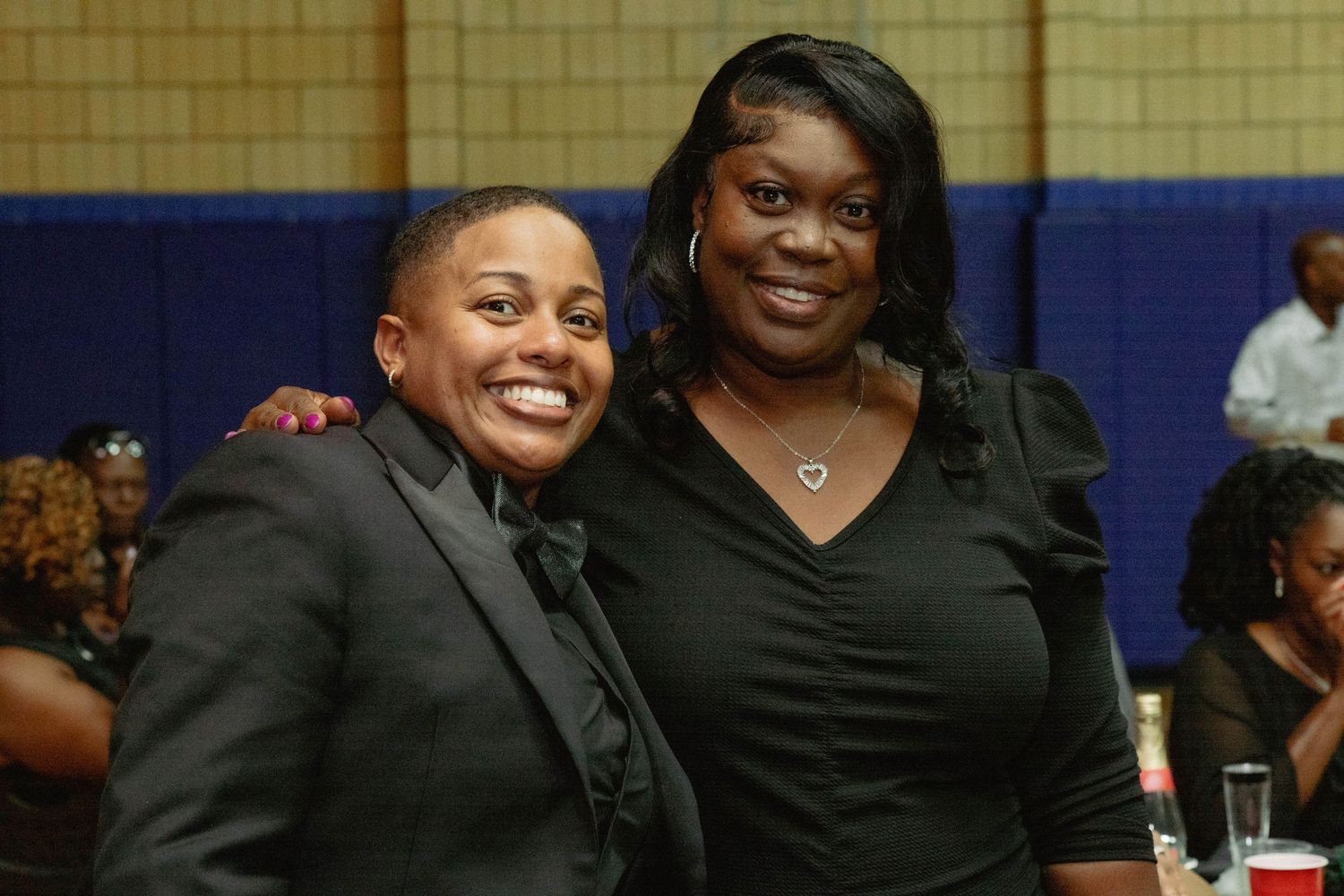 Two women smiling and posing together at a formal event, both dressed in black attire.