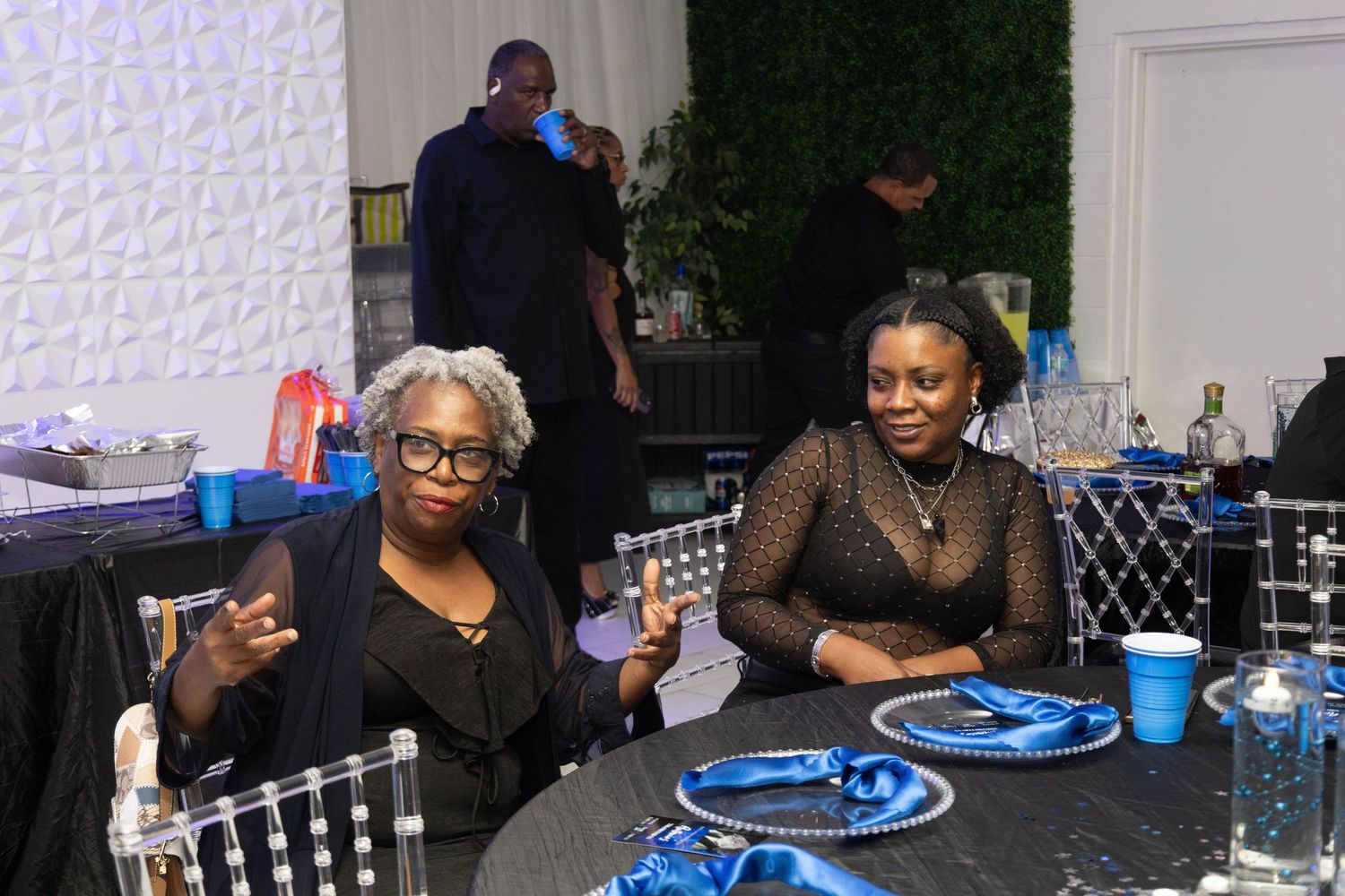 Two women seated at a decorated event table with blue and black party decorations.