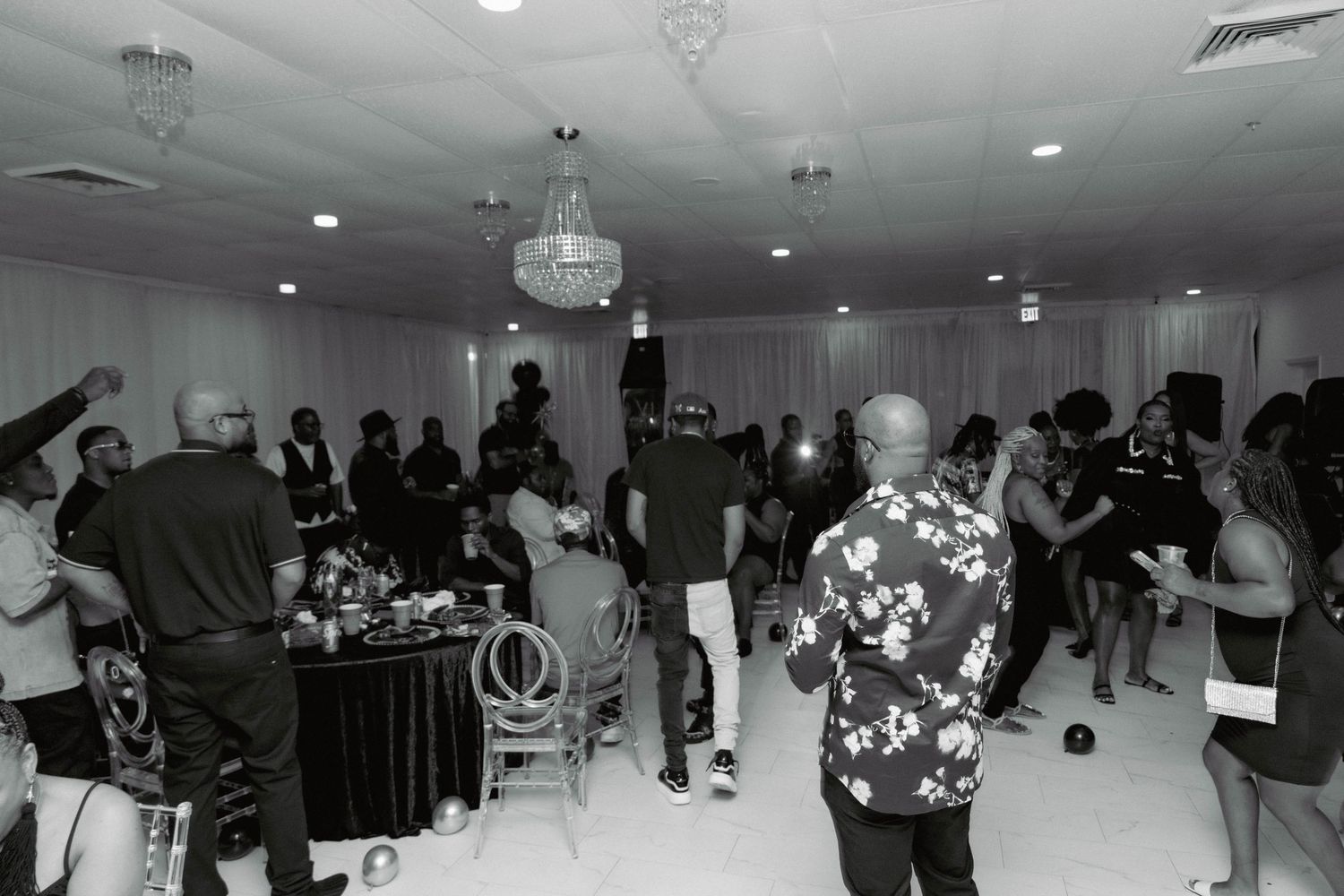 Black and white photo of guests dancing and socializing at an elegant indoor party event.