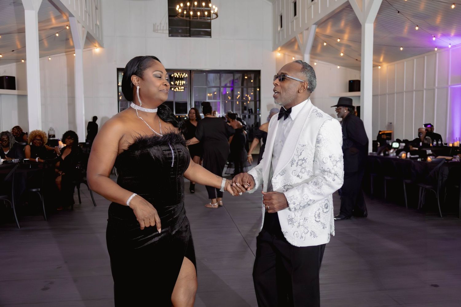 Elegantly dressed couple sharing a dance at a formal black and white themed gala event.