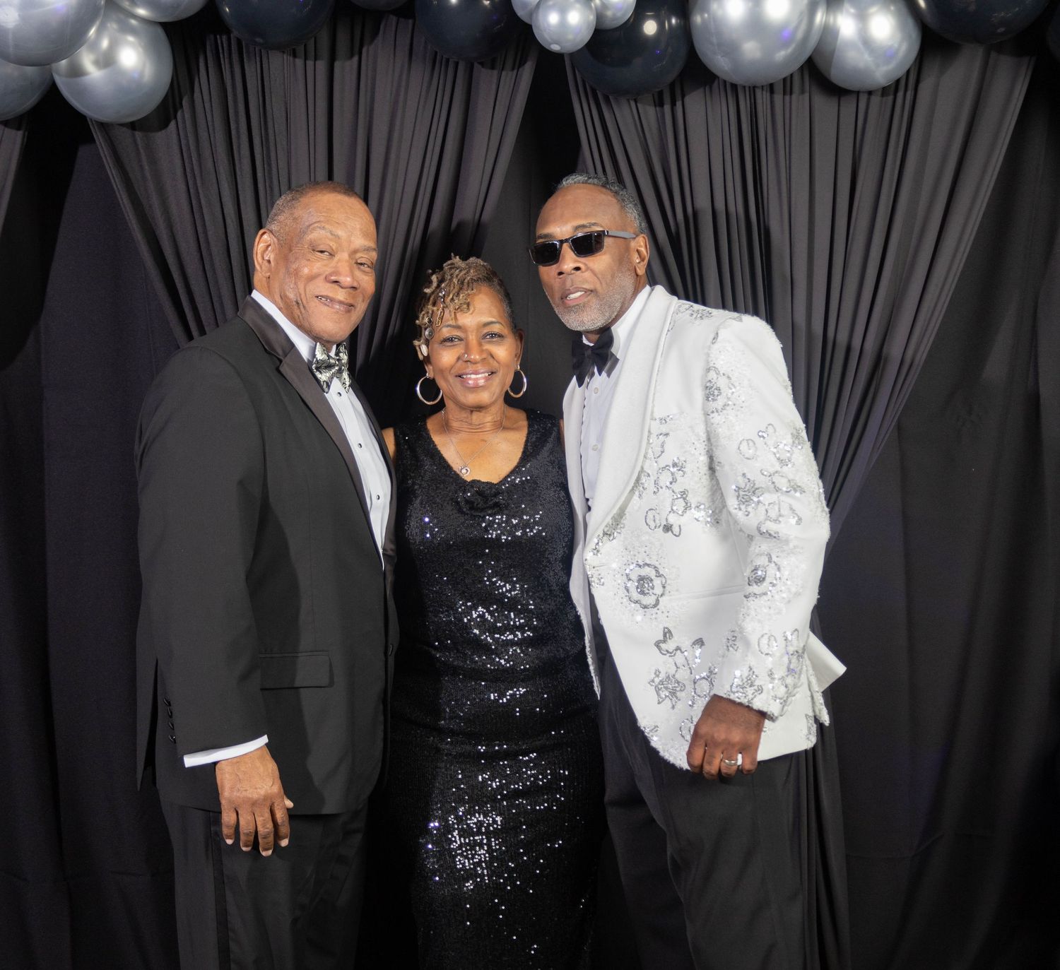 Three elegantly dressed guests posing together at a formal black and white themed gala celebration.