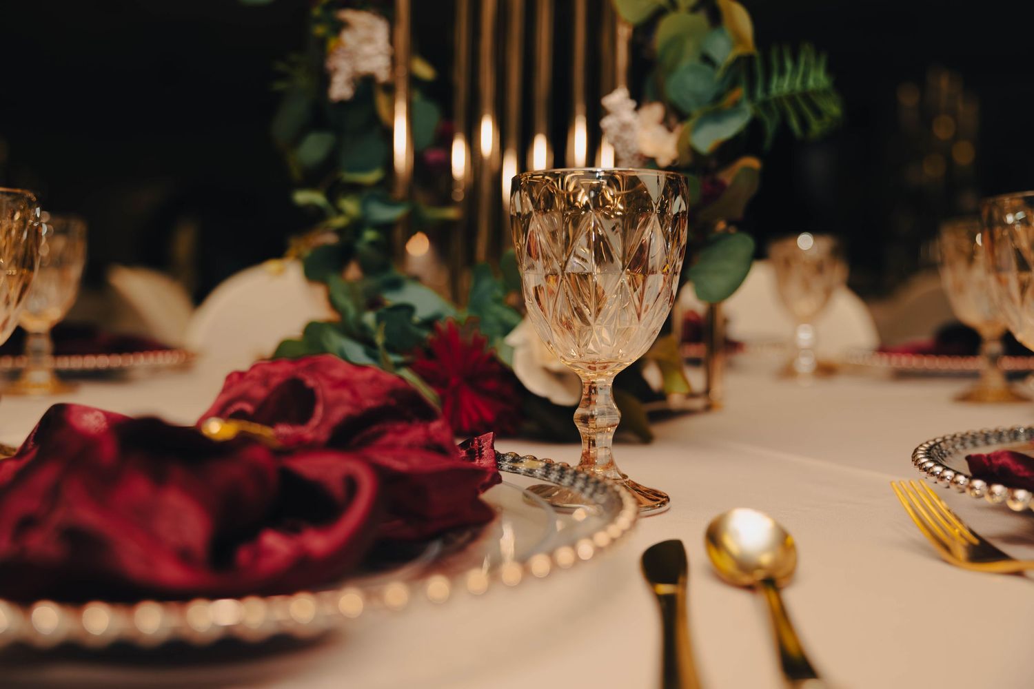 Elegant table setting with crystal glassware, red velvet napkin, and gold candlelight.