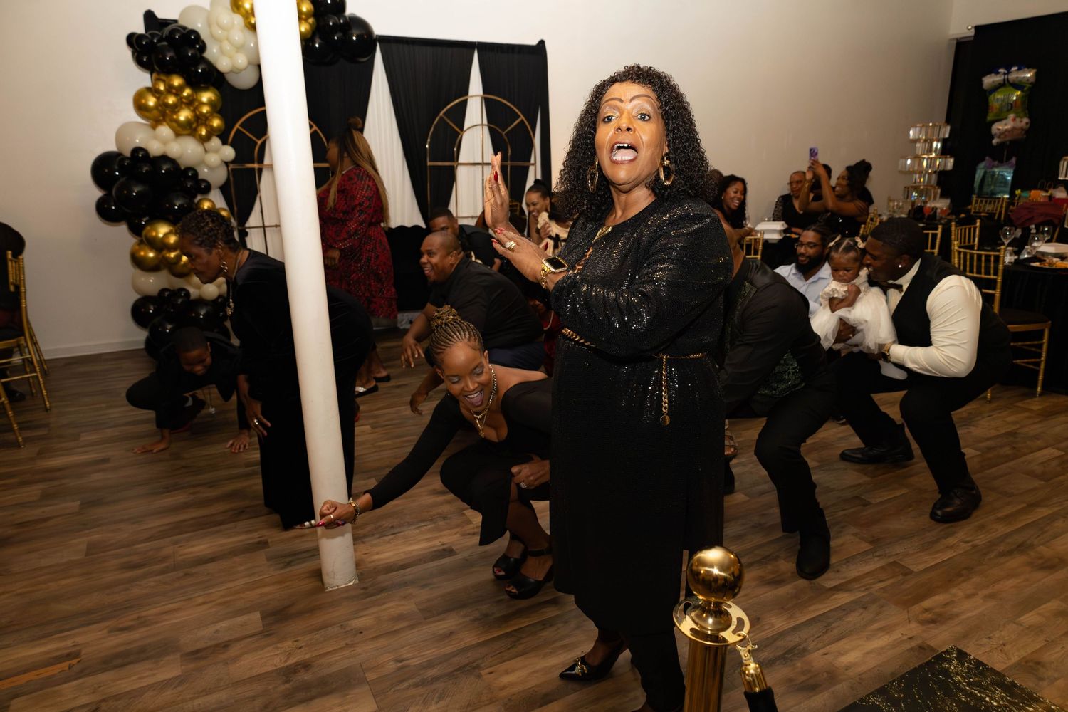 People dancing and celebrating at a black and gold themed party in an event venue.