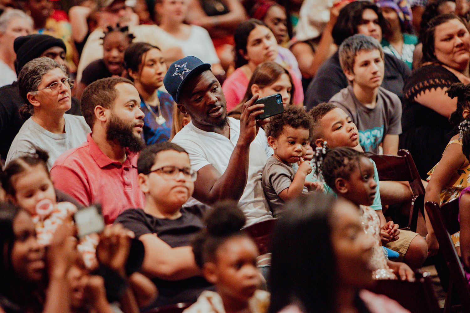Diverse crowd of families and children watch attentively at a school graduation ceremony event.