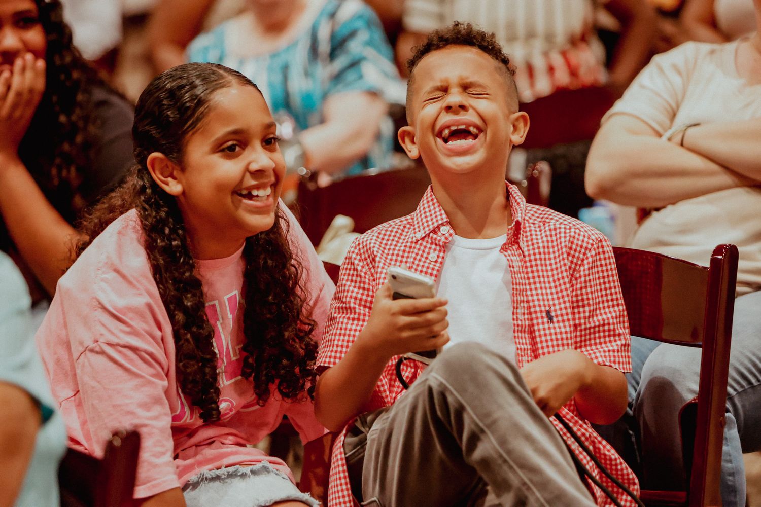 Two children laugh joyfully while sitting together at a school graduation ceremony event.