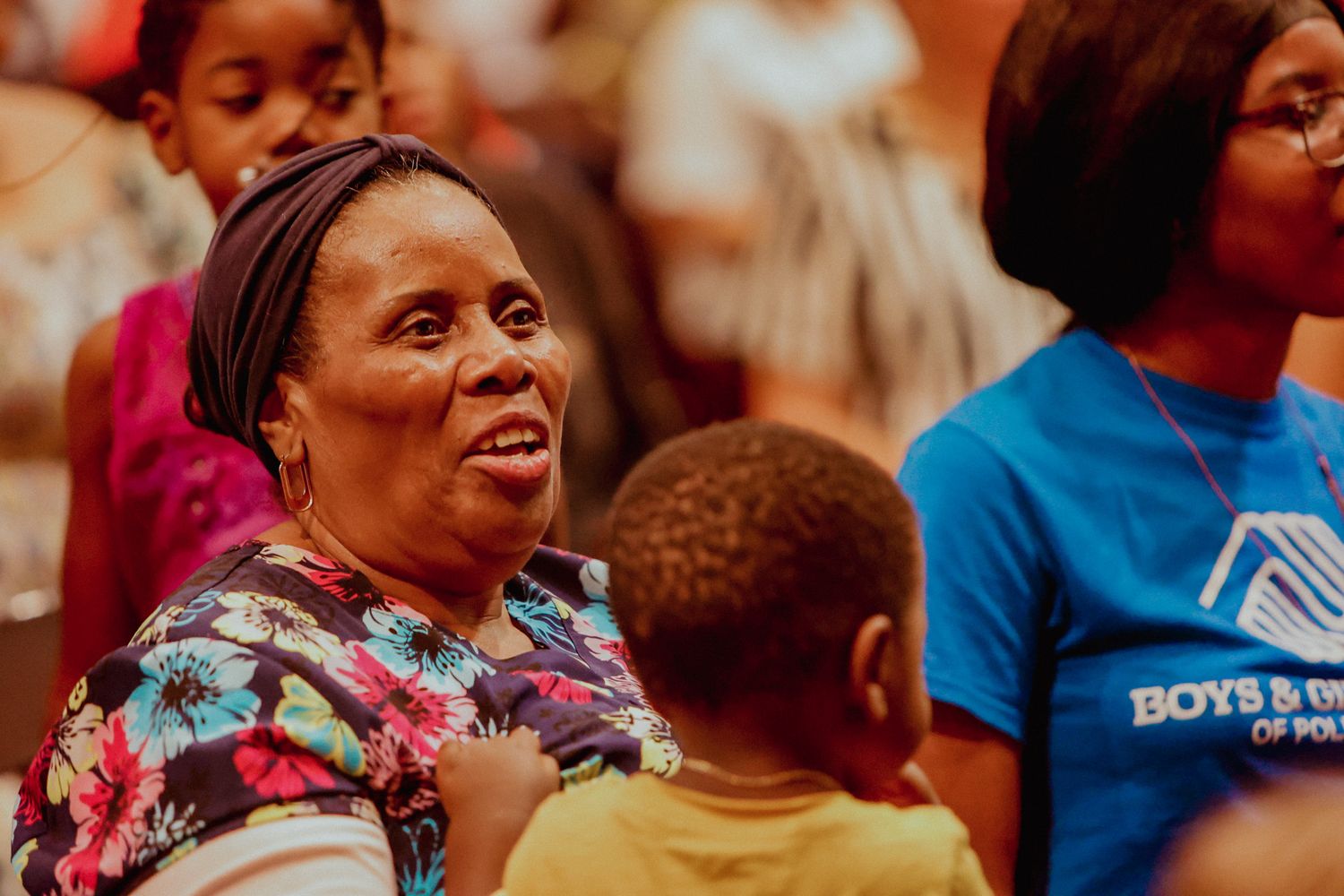 Smiling woman in floral dress enjoys a school graduation ceremony surrounded by children and families.