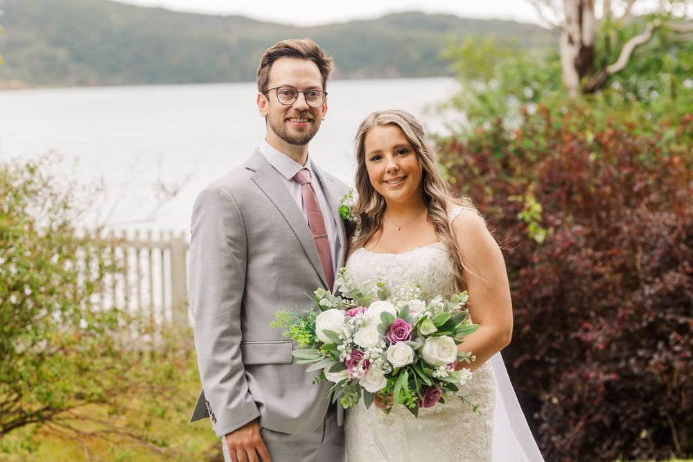 A romantic lakeside wedding celebration with soft pink bouquets and elegant gray attire against a natural backdrop.