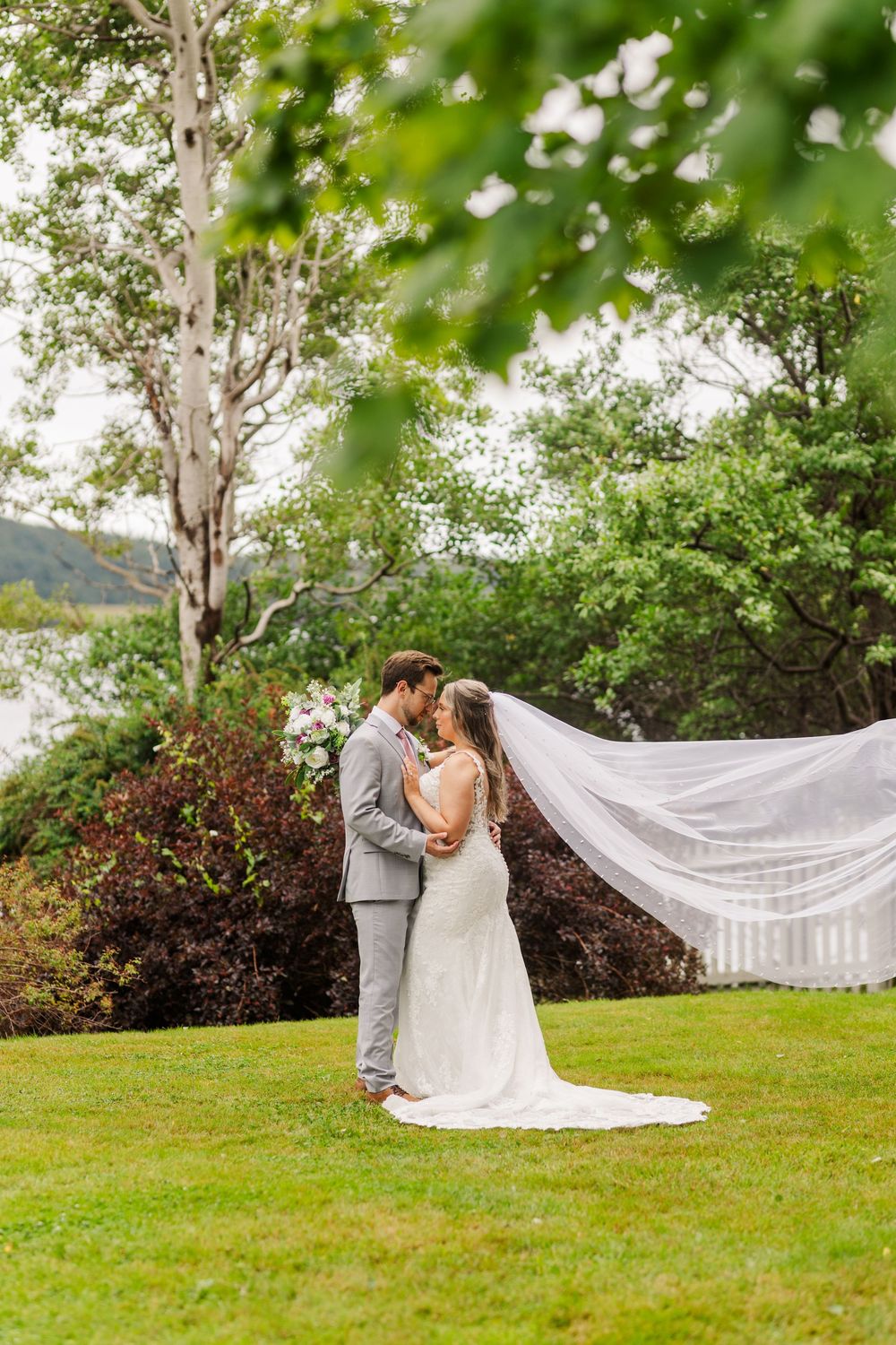 Romantic wedding photo series showing a couple embracing on a lush green lawn with a flowing white veil in the breeze.