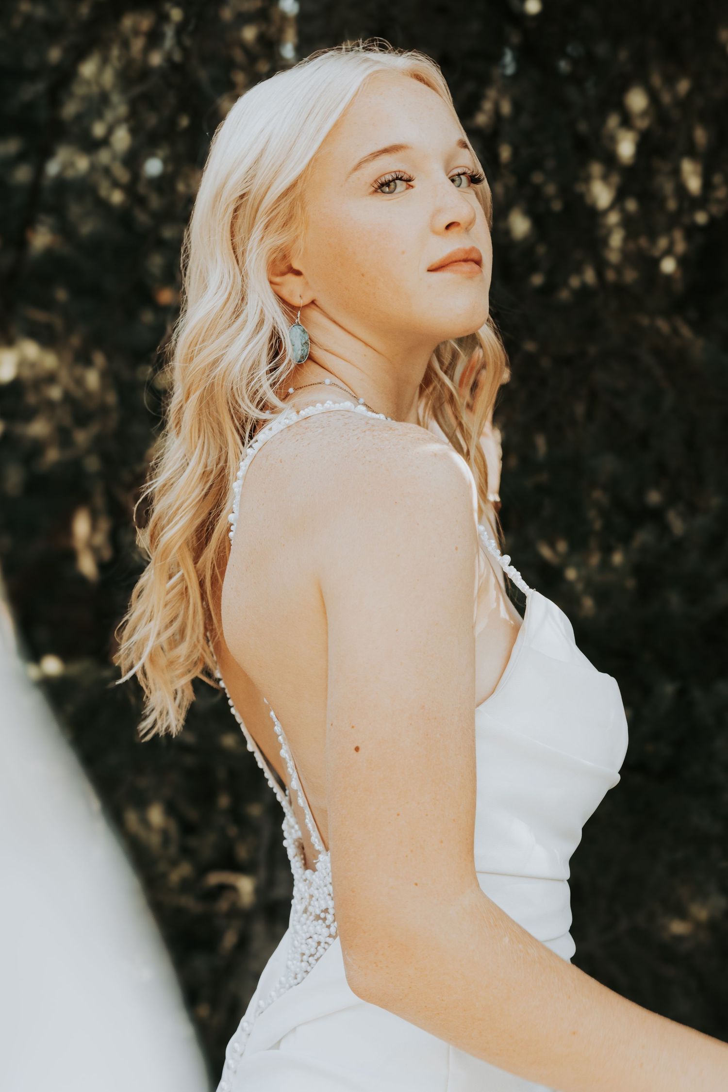 A bride in a white wedding gown with thin straps poses against a dark background while looking upward.