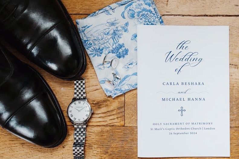 Elegant navy blue wedding invitation cards and place cards arranged with black dress shoes on wooden surface.