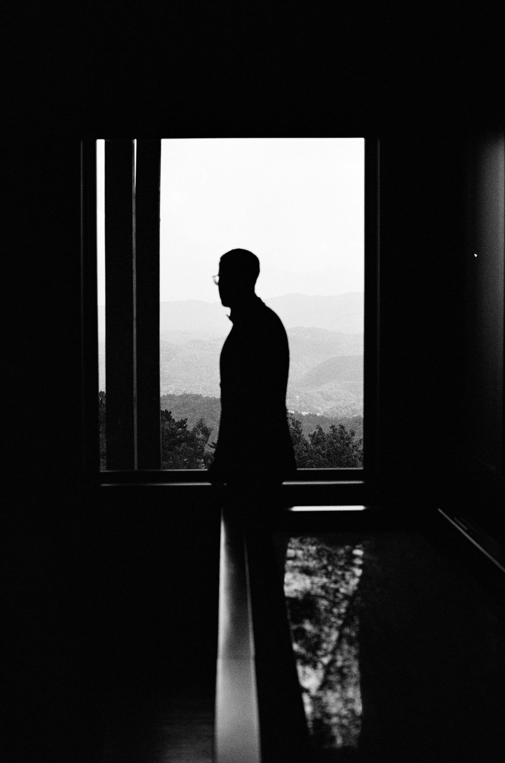 Dramatic silhouette of a figure standing by a bright window in a dark room.