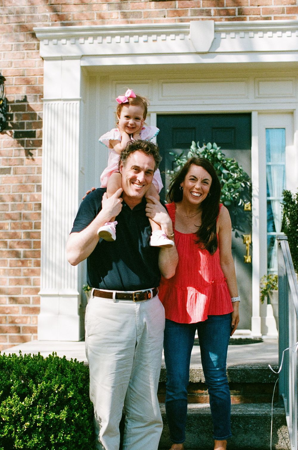 Happy family posing together on front porch steps of brick house with white columns.