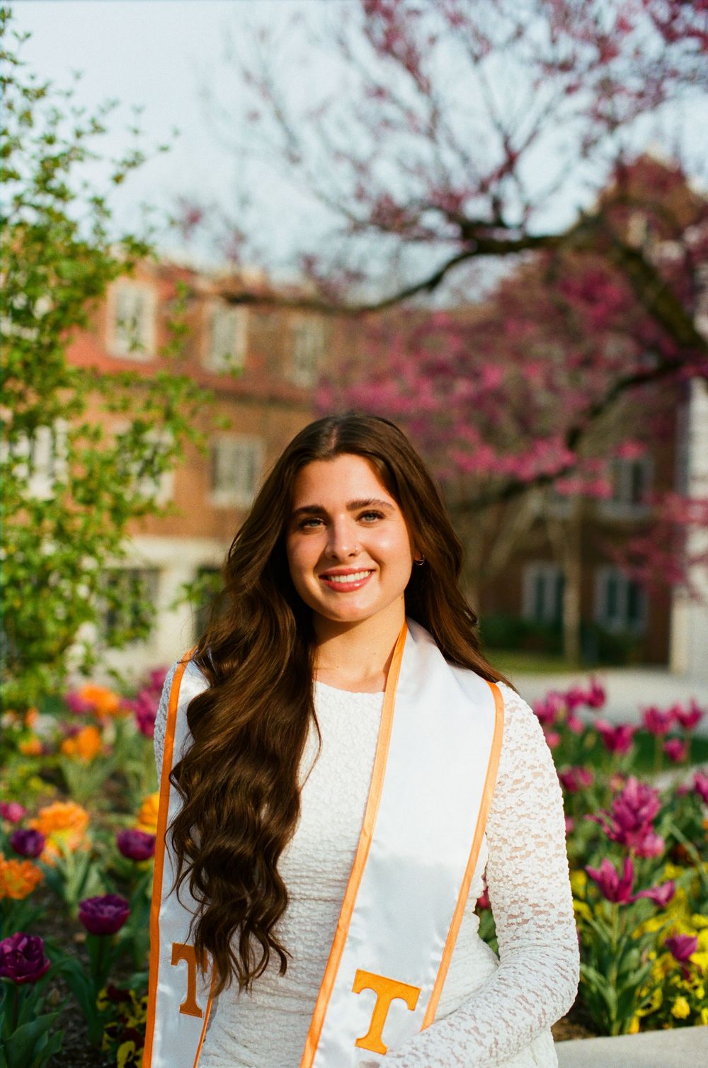 Spring graduation photos with colorful flowers and brick buildings in the background.