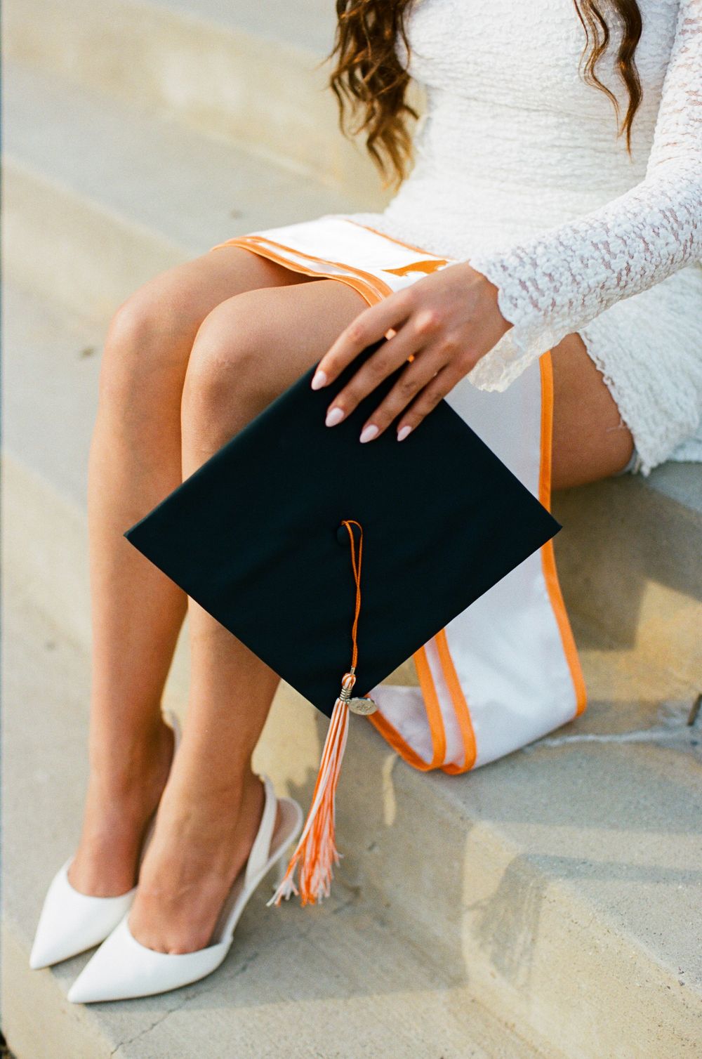 Close-up details of graduation cap and white heels against concrete steps.