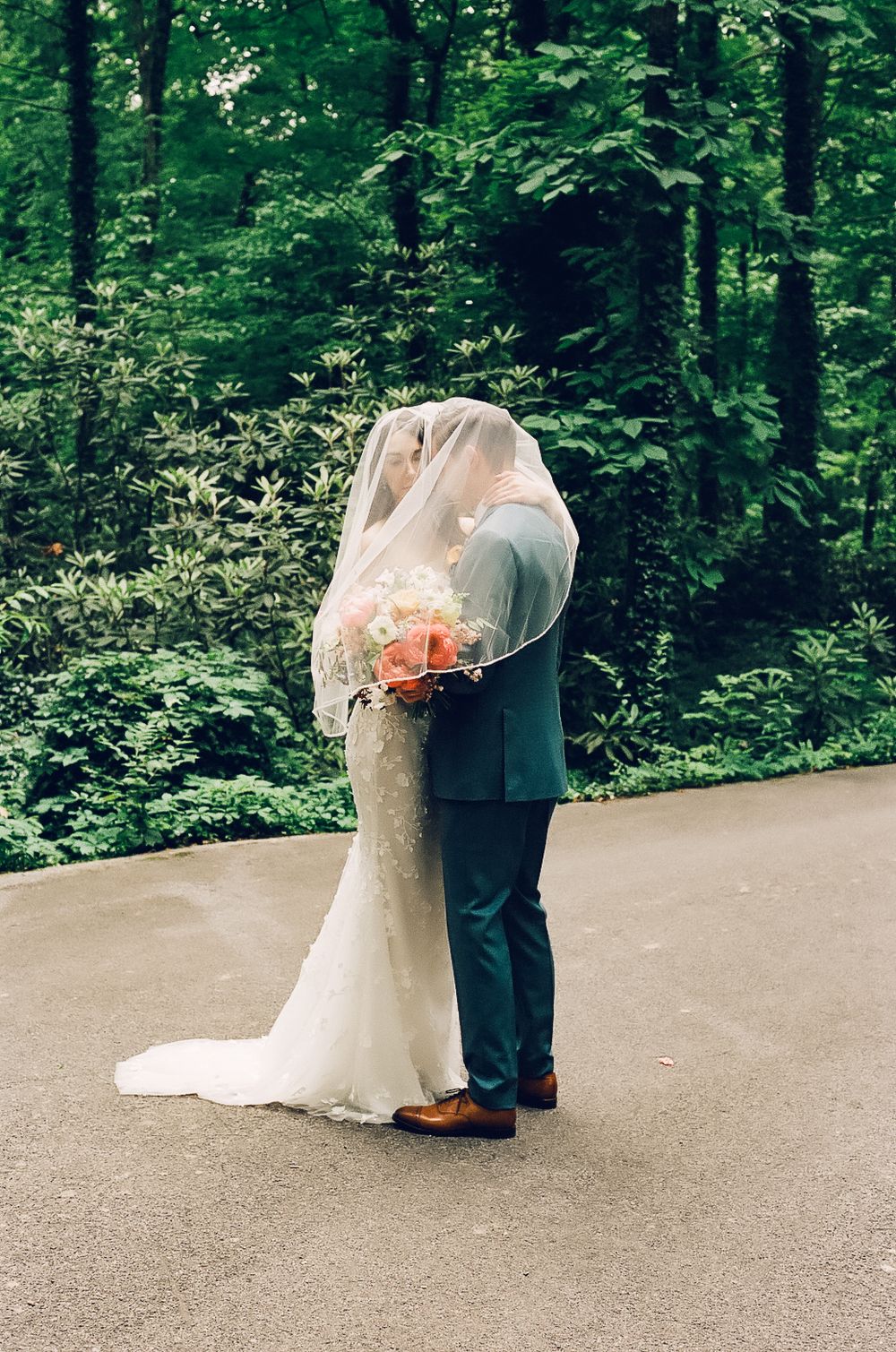 A couple shares an intimate moment under a veil on a forest path.