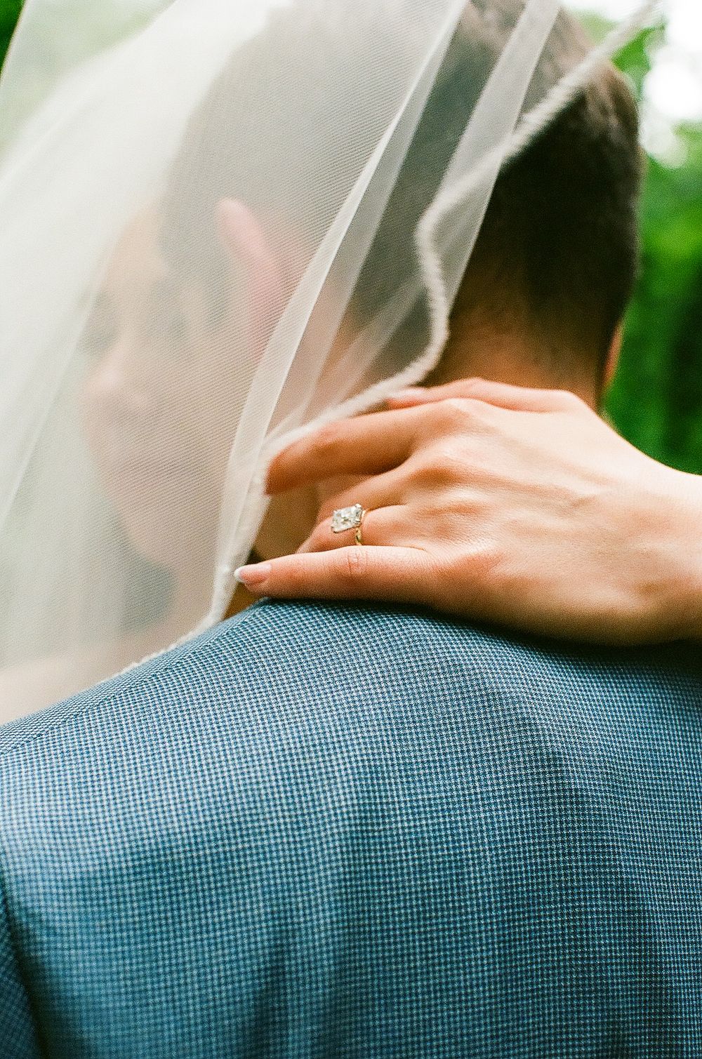 A close-up of a diamond ring as a couple embraces under a wedding veil.