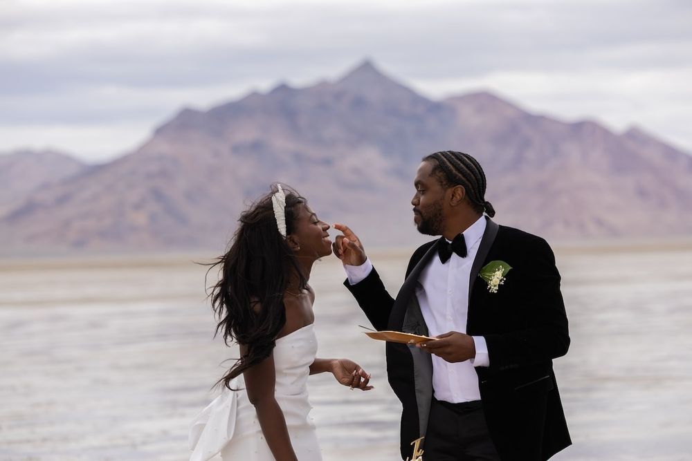 A romantic couple dances in formal attire against a scenic desert mountain backdrop at sunset.