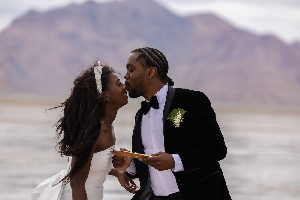 A romantic couple embraces and kisses on a beach during their outdoor wedding photoshoot session.