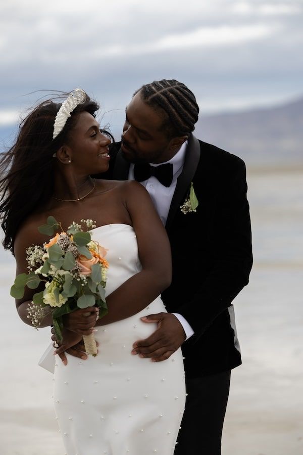 A series of four romantic wedding photos showing a couple kissing on a beach at sunset.