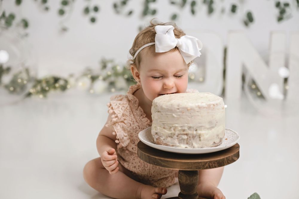 Baby reaching for white frosted cake on wooden stand during cake smash session.