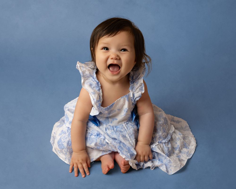Baby in blue and white dress against blue backdrop during portrait session.