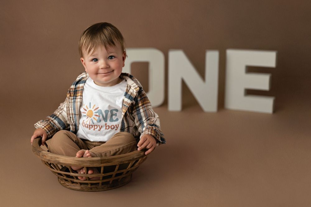 Baby in brown baseball glove sits on brown backdrop during milestone portrait session.