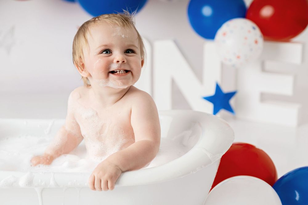 Baby in patriotic red white and blue themed photo shoot with balloons and stars in studio setting.