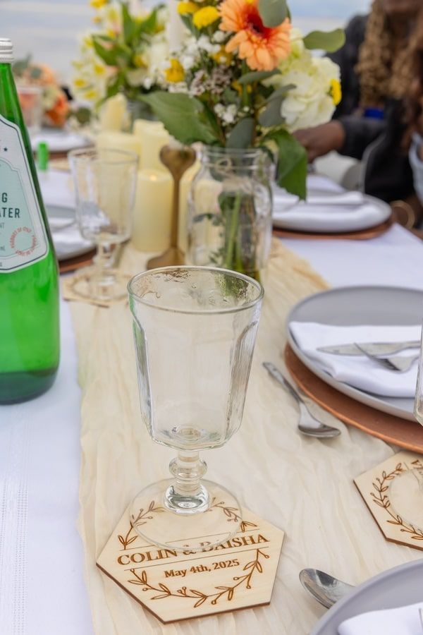 Table setting at a wedding reception with personalized wooden coasters and spring floral centerpieces.