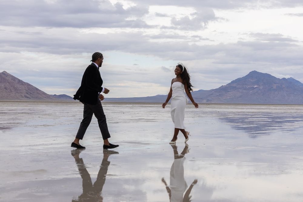 A couple in wedding attire dances on the reflective surface of the Bonneville Salt Flats with mountains in the background.