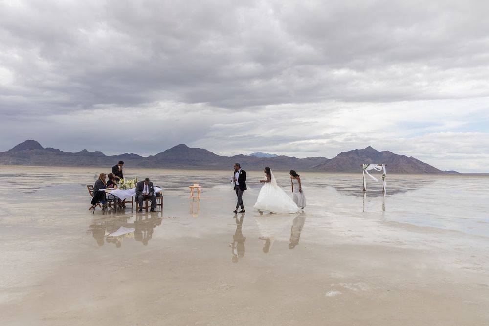 A wedding photoshoot takes place on the reflective surface of Bonneville Salt Flats with mountains in the background.