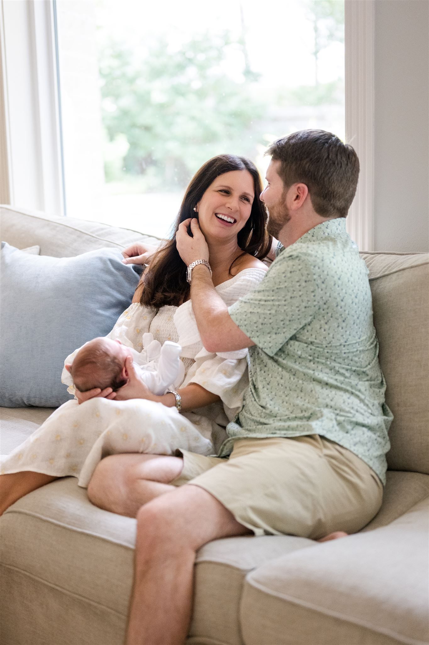 A loving couple shares tender moments while relaxing together on a beige couch in a bright sunlit room.