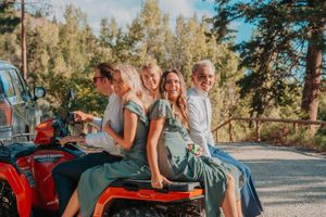 People sitting together on a red ATV in a sunny wooded area during golden hour.