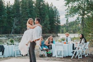 Outdoor wedding celebration with dining tables set up near evergreen trees at sunset.