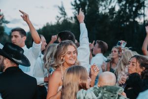 Crowd of joyful wedding guests dancing with raised arms at an outdoor celebration with dusk lighting.