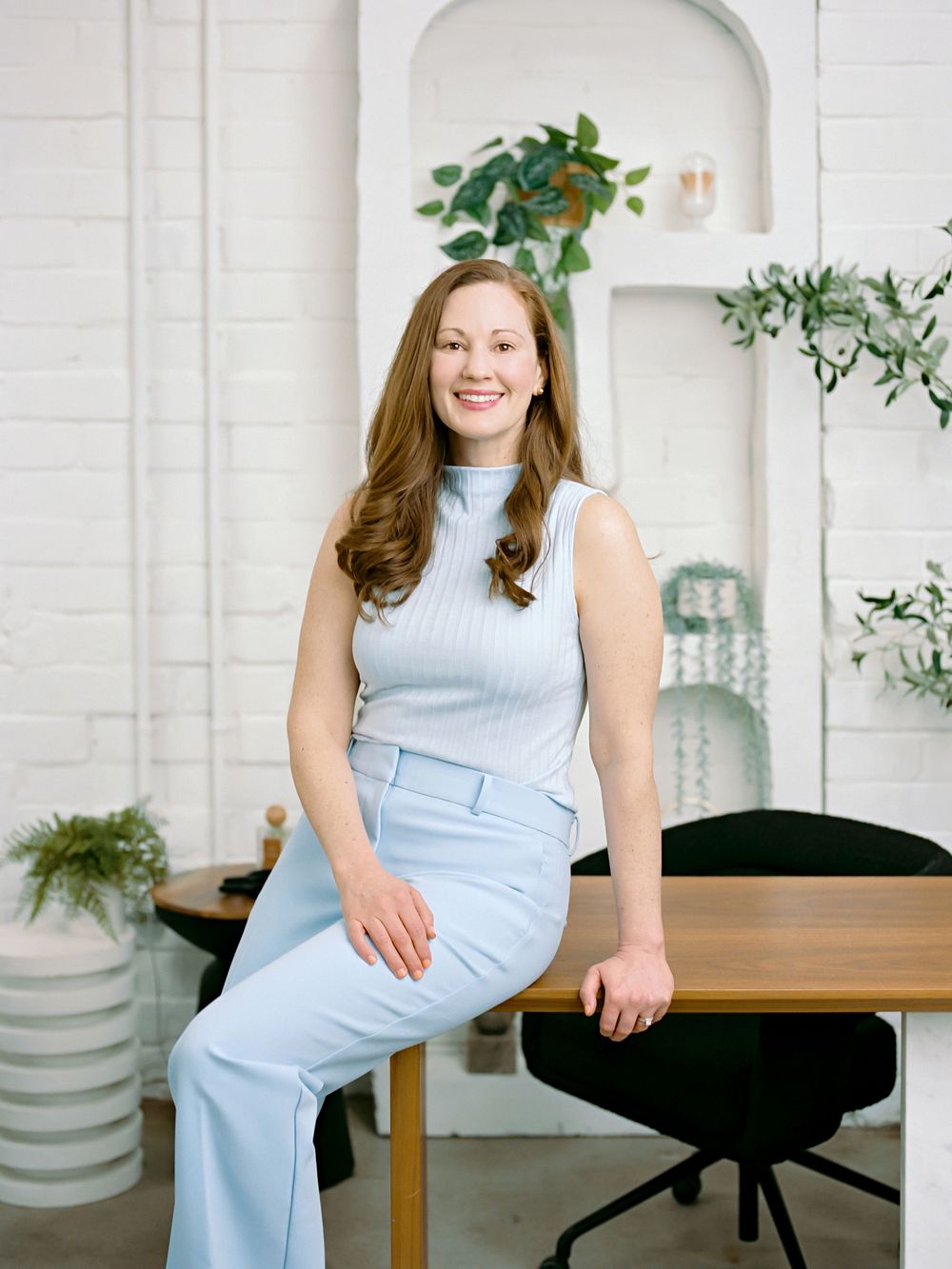 Professional lifestyle portrait in a bright modern home office with indoor plants and blue monochromatic outfit.