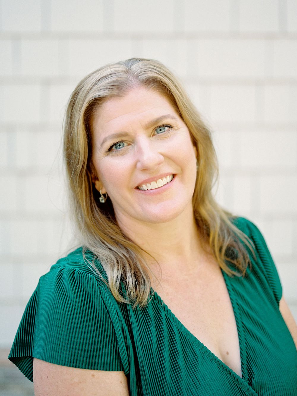 Professional headshot portraits with emerald green blouse against light neutral background.