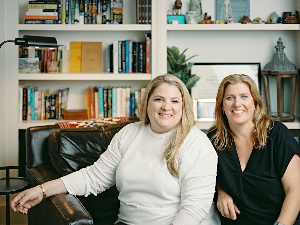 Two people sit together on a couch in front of built-in bookshelves and home decor.