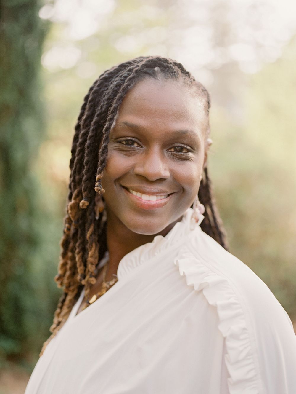 Portrait photograph featuring long braided hair and a white ruffled blouse against a soft natural background.