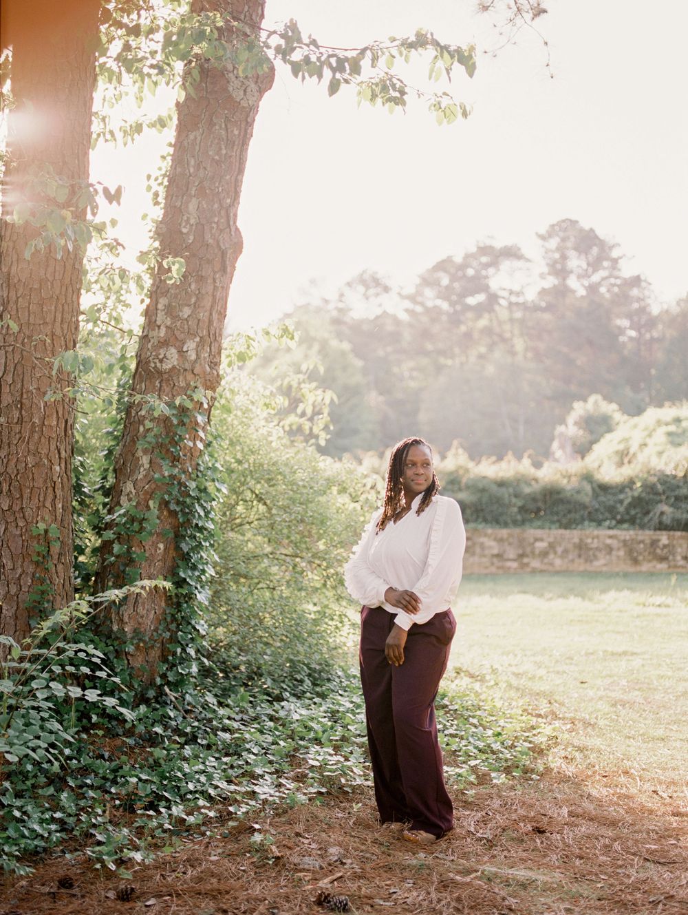 A scenic forest engagement photoshoot shows a couple in casual attire embracing among trees during golden hour.