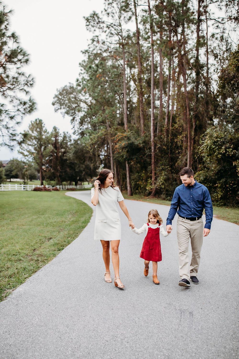 A tender family walking together on a winding path surrounded by tall pine trees and green grass on a sunny day.