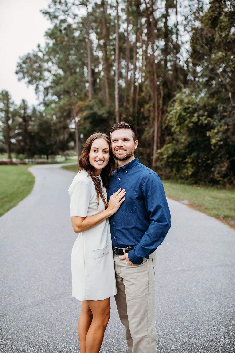 A couple shares a tender moment on a winding path surrounded by tall pine trees.