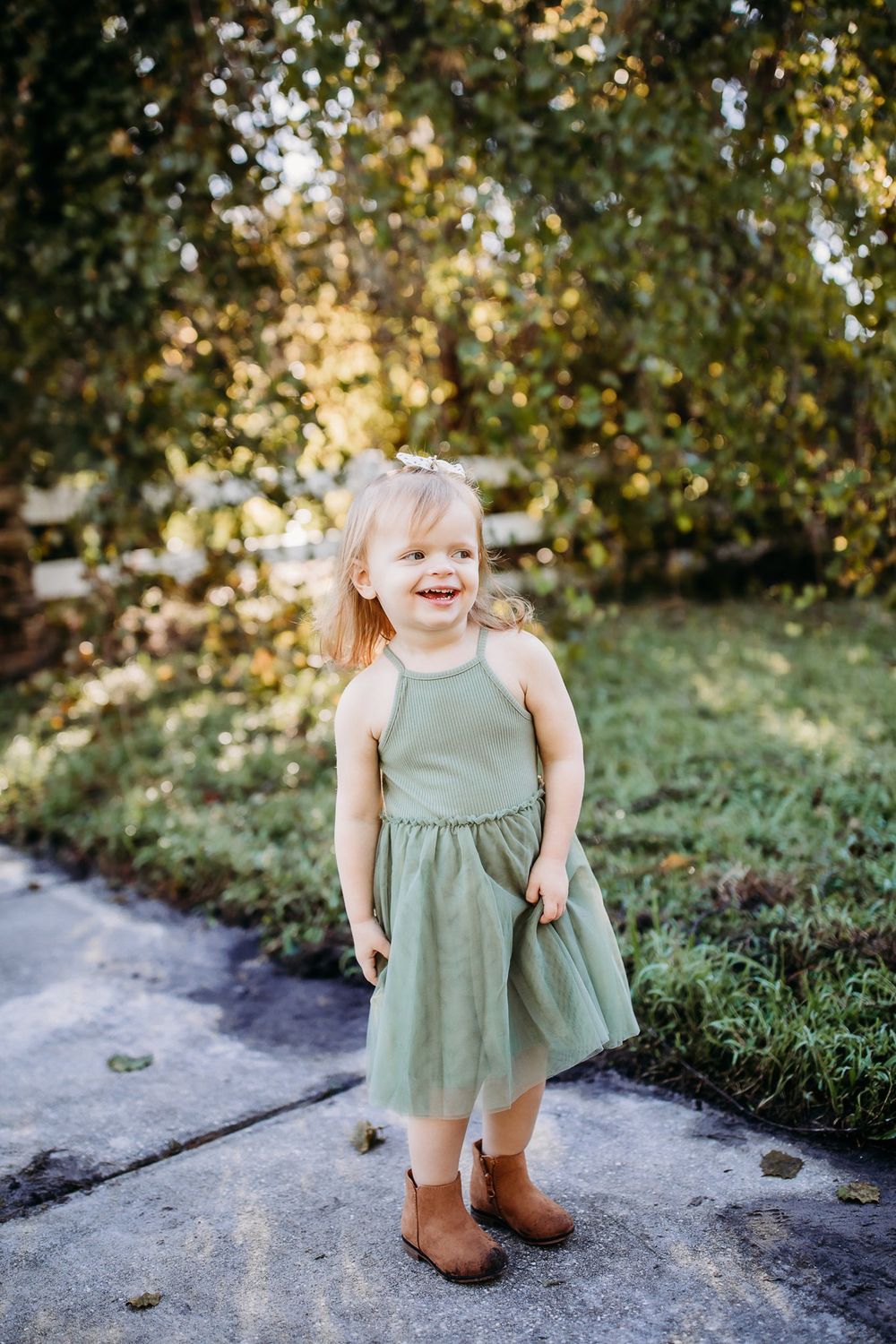 Small child in a mint green dress and brown boots twirling on a concrete path outdoors.