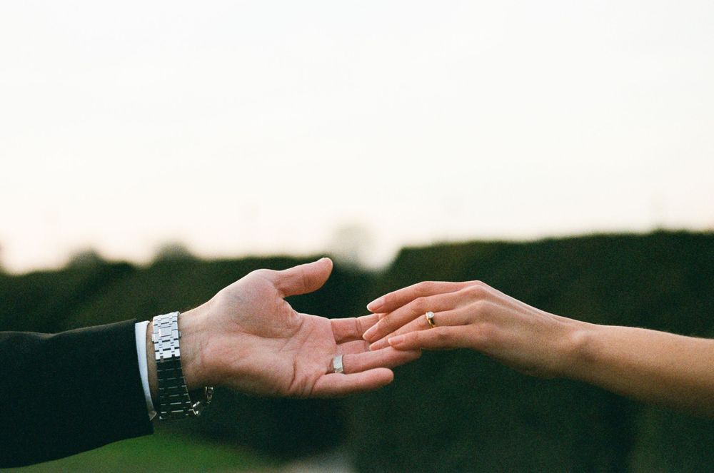 Two hands reaching towards each other with one palm open against a dark moody background with shallow depth of field.