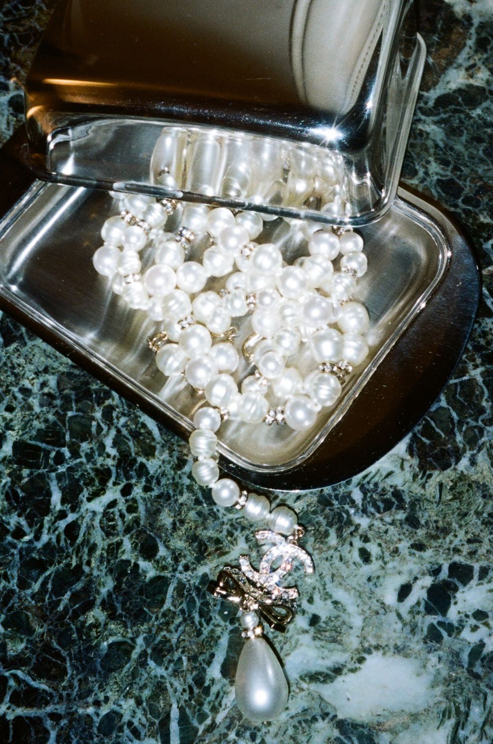 Pearl earrings reflecting on green marble surface create an elegant mirrored composition in jewelry photography.
