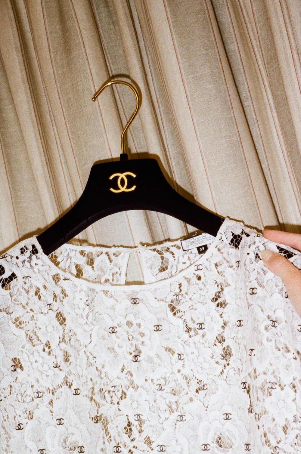 Several white lace garments displayed on black Chanel branded hangers against a light colored curtained background.