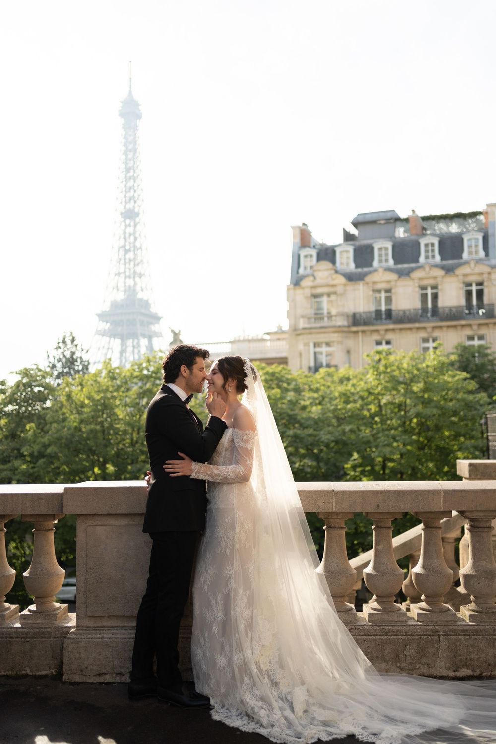 A romantic wedding photo session on a Paris balcony with the Eiffel Tower visible in the background at sunset.